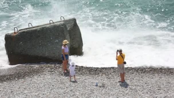 Uomo fotografare la sua famiglia in piedi in spiaggia di ghiaia, mare sullo sfondo — Video Stock