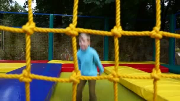 Joven feliz niño saltando en trampolín inflable en parque de atracciones detrás de la red — Vídeos de Stock