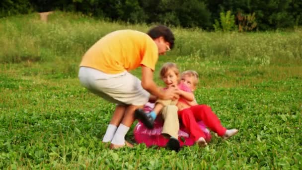 Homem, menino e menina fazem o tolo sentado em uma poltrona inflável das crianças no campo no parque — Vídeo de Stock