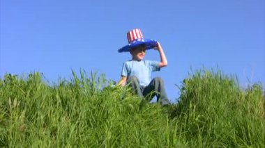 Amerikan bayrağı şapkalı çocuk çimenlerin üzerinde oturur ve dünya tutar