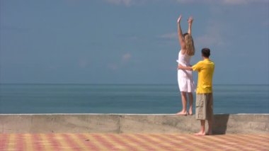 Deniz kenarında kaldırdı elleriyle kadın, adam onu tutar.