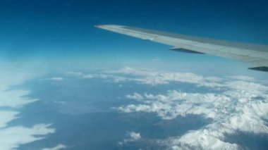 Bir uçak penceresinden görünümü: dağlar üzerinden bir uçak kanadı. Zaman atlamalı