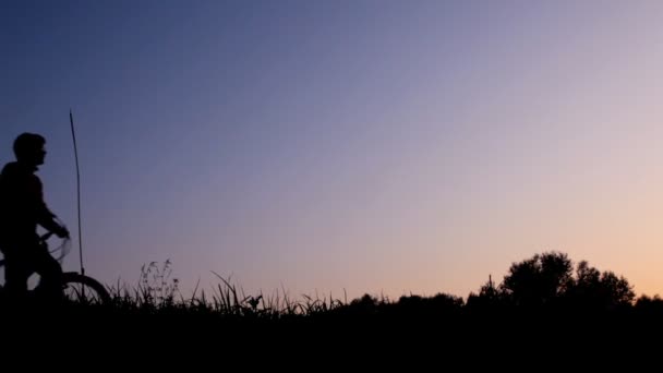 Männersilhouette läuft mit Fahrrad gegen den Himmel — Stockvideo