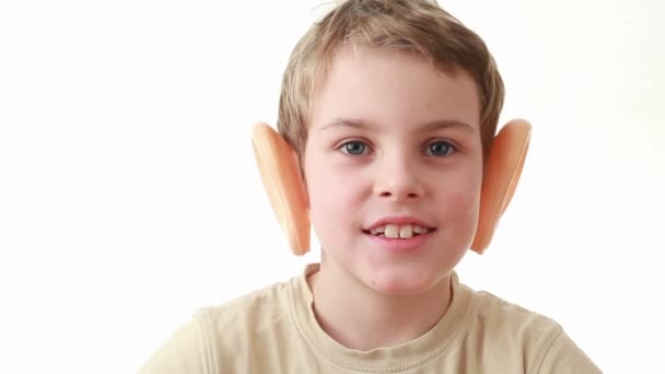 Boy with big plastic ears, sitting on a white background, turns his head — Stock Video