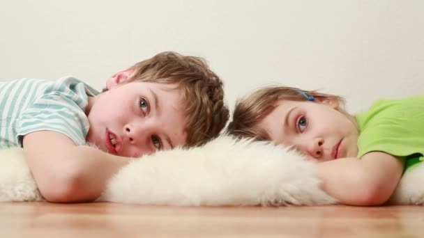 Niño y niña se acuestan en el suelo sobre una alfombra peluda — Vídeo de stock