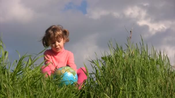Menina com globo terrestre senta-se na grama contra o céu — Vídeo de Stock