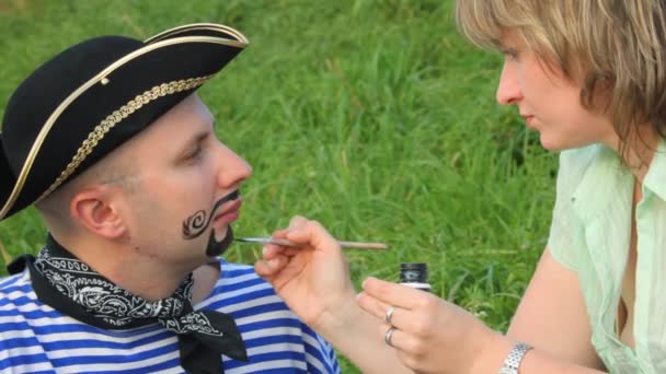 Женщина рисует усы на лице мужчины в пиратском костюме — стоковое видео