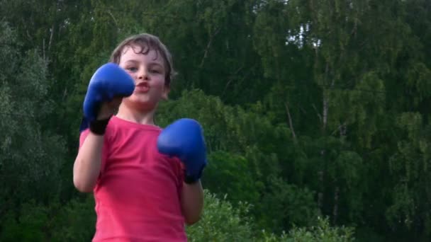 Мальчик в боксёрских перчатках занимается карате в парке — стоковое видео