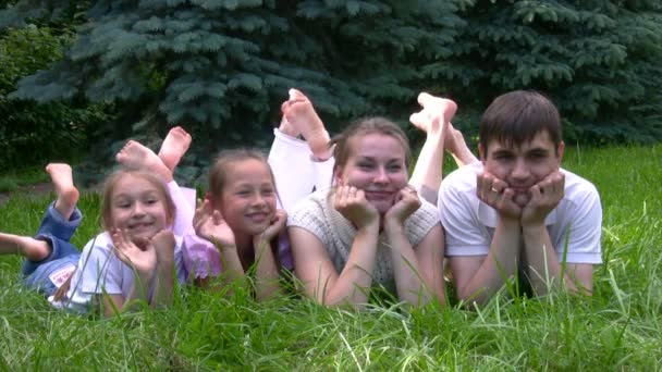 Familie liggen op gras en hangertjes gekruiste benen in park — Stockvideo