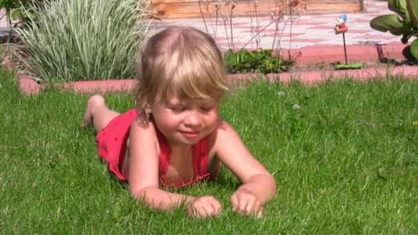 Retrato de linda niña acostada sobre hierba verde en la salida y cuelga las piernas — Vídeo de stock