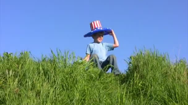 Garçon en chapeau drapeau américain est assis sur l'herbe et tient globe — Video