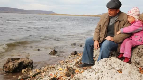 Тато з дочкою сидіти на камінь на березі річки — стокове відео