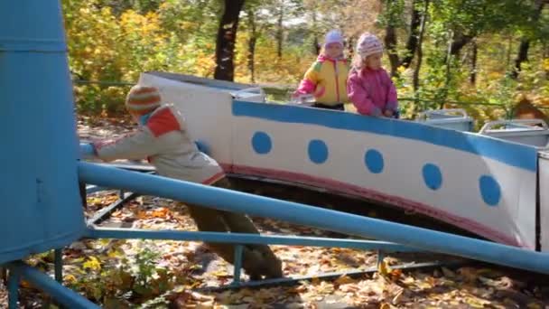 Menino empurrando no carrossel com meninas no playground — Vídeo de Stock