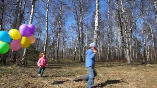 Boy holds bunch of balloons and little girl runs around in spring forest — Stock Video