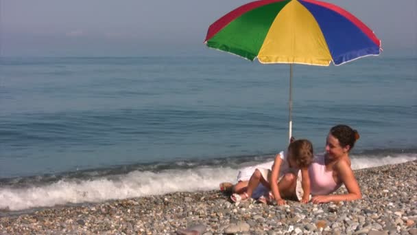 Mother with daughter under umbrella on shore — Stock Video