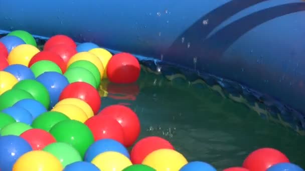 Рука ребенка, подбирающего разноцветные шарики, плавающие в надувном бассейне — стоковое видео
