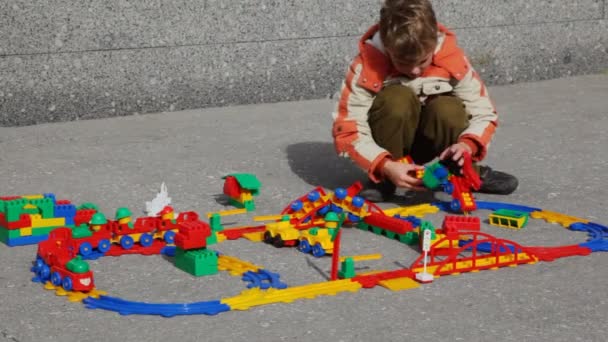 Boy collects structure of toy railway in street — Stock Video