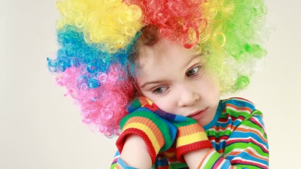 Chica en una ridícula peluca multicolor y llamativa camiseta a rayas golpea las manos sobre su cara — Vídeos de Stock