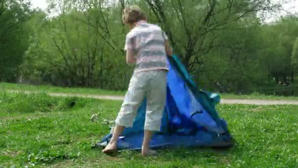 De jongen stelt tent op een glade in zomerdag. time-lapse. — Stockvideo