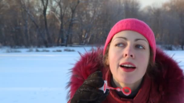 Женщина надувает мыльные пузыри в зимнем парке — стоковое видео