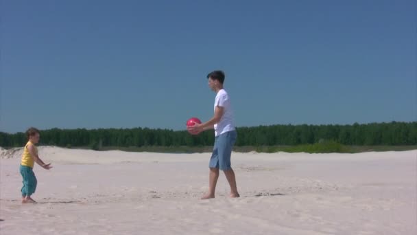 Man och pojke leker med boll på stranden — Stockvideo