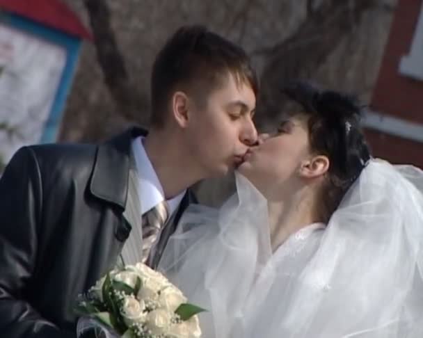 Kissing bridegroom and bride stands on street — Stock Video