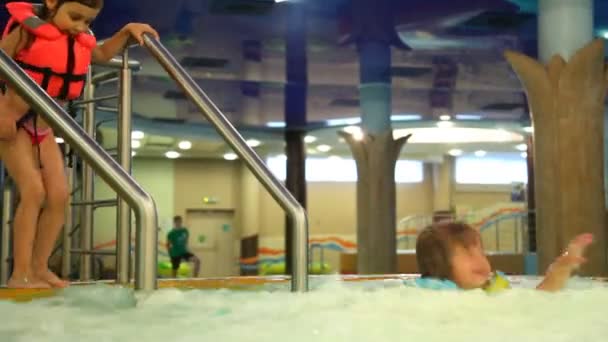 Jongen en meisje springen één voor één in jacuzzi bruisend water in waterpark — Stockvideo