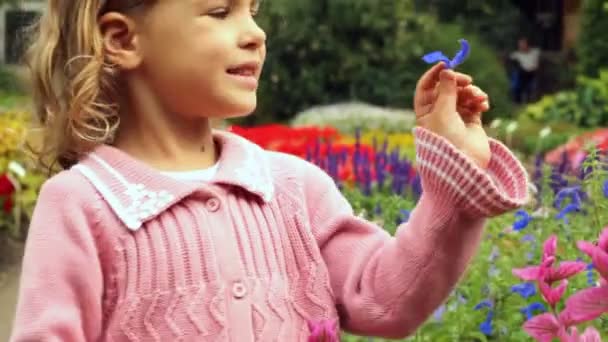 Little girl holds in hand violet petal and examines it, standing in park — Stock Video