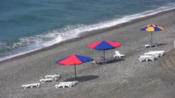 Guarda-chuvas e camas na praia de seixos com surf no mar — Vídeo de Stock