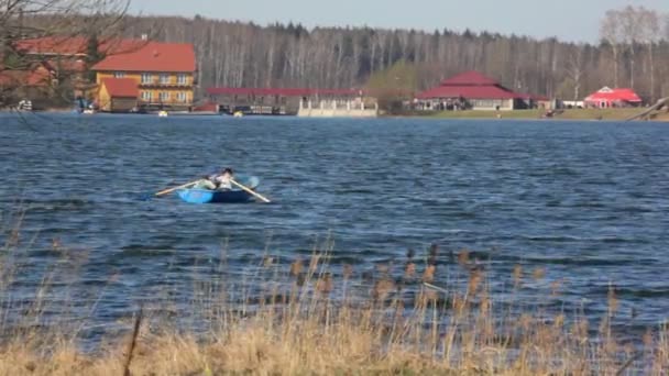 Two boys oars in boat on river, buildings and forest in background — Stock Video