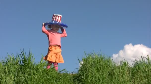 Flicka i amerikanska flaggan hatt står på fältet mot himlen — Stockvideo