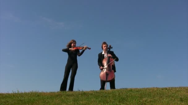 Man en vrouw speelt cellos op heuvel — Stockvideo