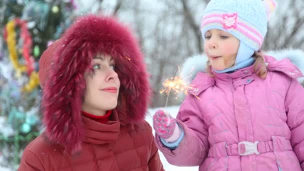 Мать и ее маленькая дочь с бенгальским огнем против рождественской елки на открытом воздухе — стоковое видео