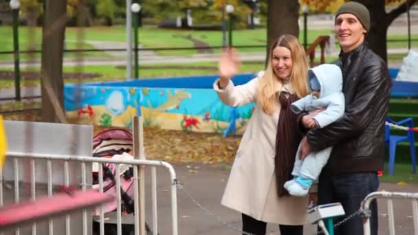 Счастливая семья с ребенком стоит в парке аттракционов — стоковое видео