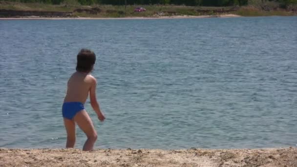 Niño en la playa arrojando piedra en el río — Vídeo de stock