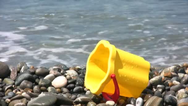 Cubo amarillo para niños en la playa rocosa — Vídeos de Stock