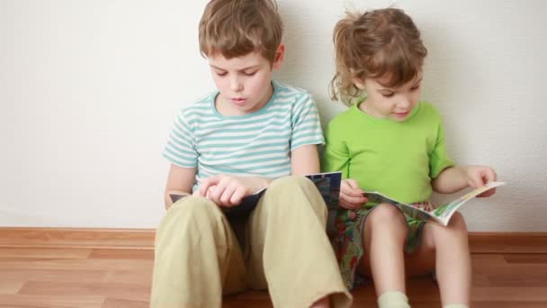 Garçon et fille assis sur le sol appuyé contre le mur et lire — Video