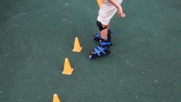 Boy in rollers puts counters on asphalt and passes between them — Stock Video