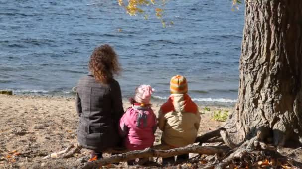 Mujer y niños se sientan bajo el árbol en el banco — Vídeos de Stock