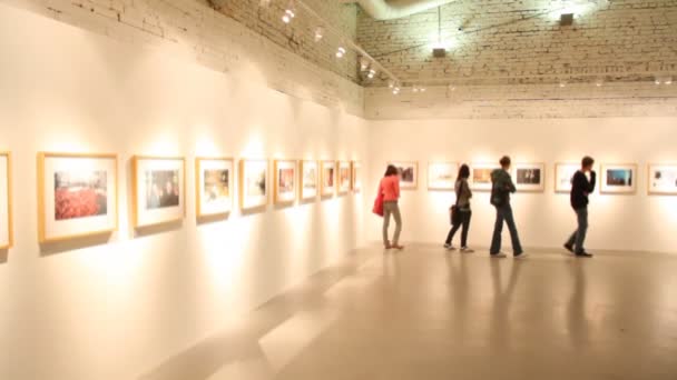 Посетители прогуливаются и смотрят на картины в выставочном зале — стоковое видео