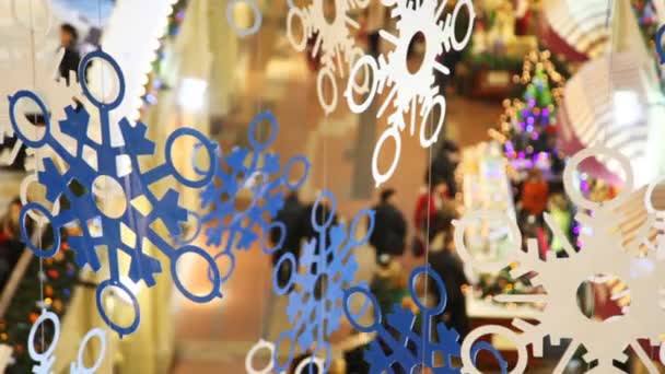 Close up paper snowflakes on cords, against shopping centre pavilions — Stock Video
