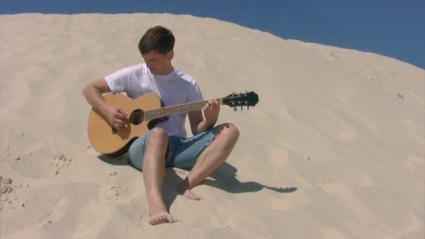 Człowiek siedzi na plaży i gra na gitarze — Wideo stockowe