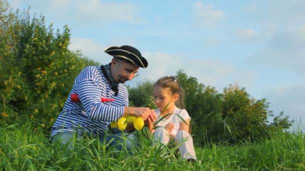 Человек в пиратском костюме и девушка сидит на траве и делает пуделя из воздушного шара — стоковое видео