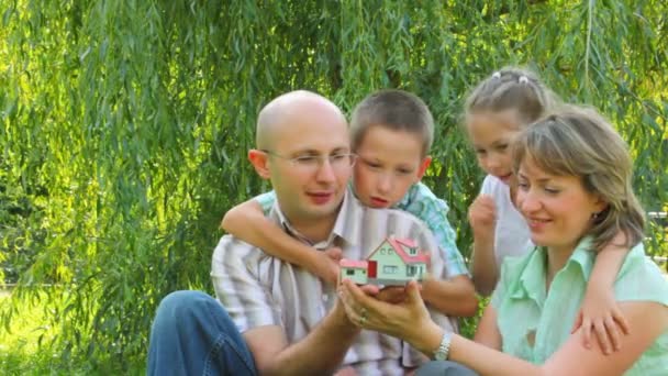 Familie van vier zit in het park en het nemen van goede kijken naar speelgoed huis — Stockvideo