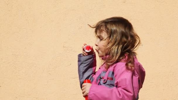 Mädchen bläst Immobilienblasen im Hof seitwärts auf — Stockvideo