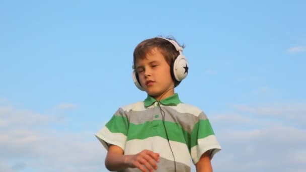 Мальчик с закрытыми глазами слушает музыку через наушники и танцует — стоковое видео