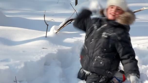 少年は歩くし、冬の木に雪玉を果たしています。 — ストック動画