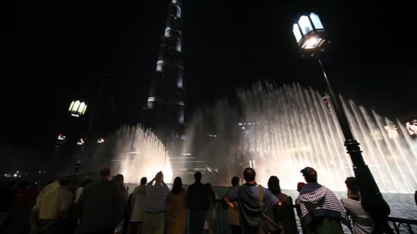 Turistas olham para fontes mostram perto do arranha-céu noturno Burj Khalifa em Dubai, Emirados Árabes Unidos . — Vídeo de Stock