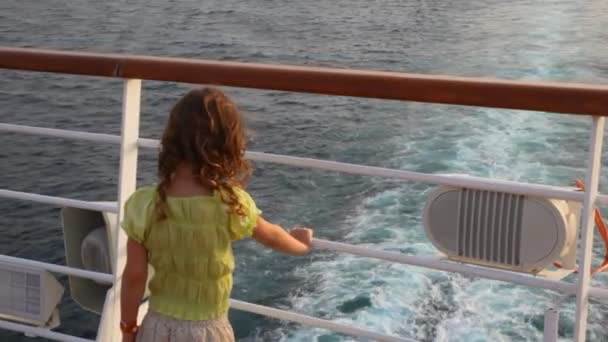 Menina fica na popa do navio de cruzeiro e olha para o mar — Vídeo de Stock