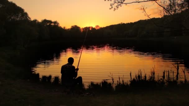 Vista trasera del hombre sentado cerca del agua y la pesca — Vídeos de Stock